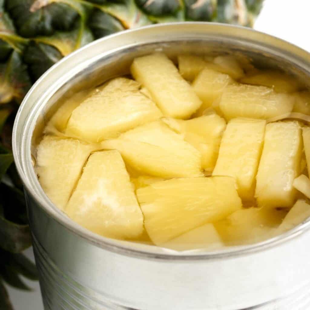 open can of store bought pineapple chunks next to a whole pineapple