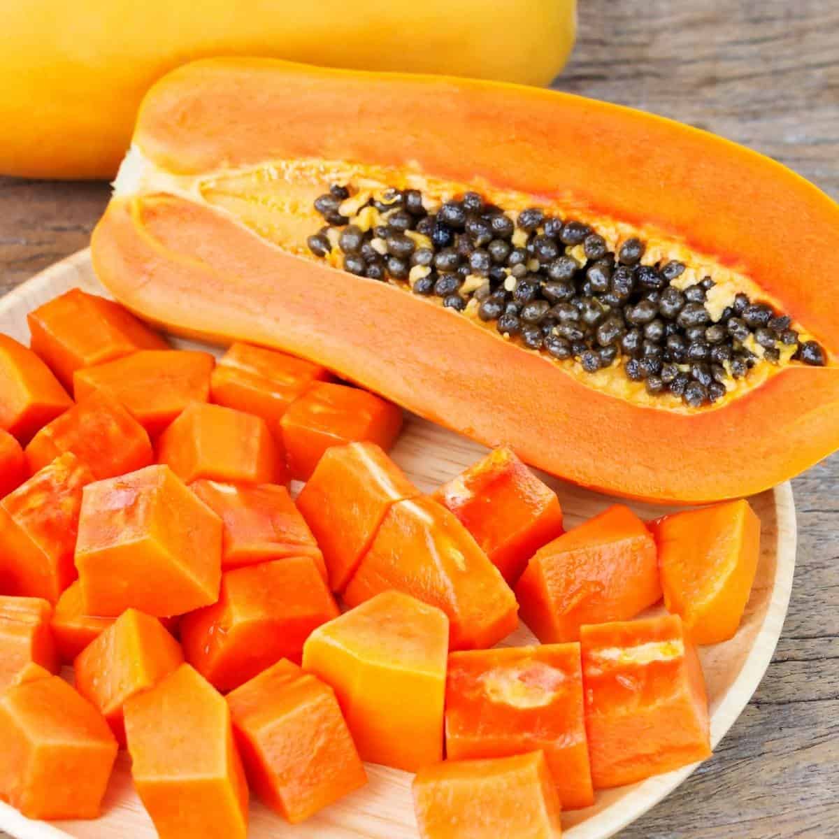 sliced papaya on a plate next to a papaya half with seeds