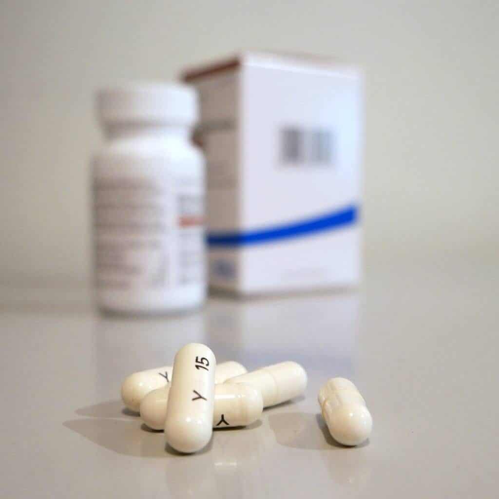 bottle of medicine in the background with 5 capsule pills in the foreground