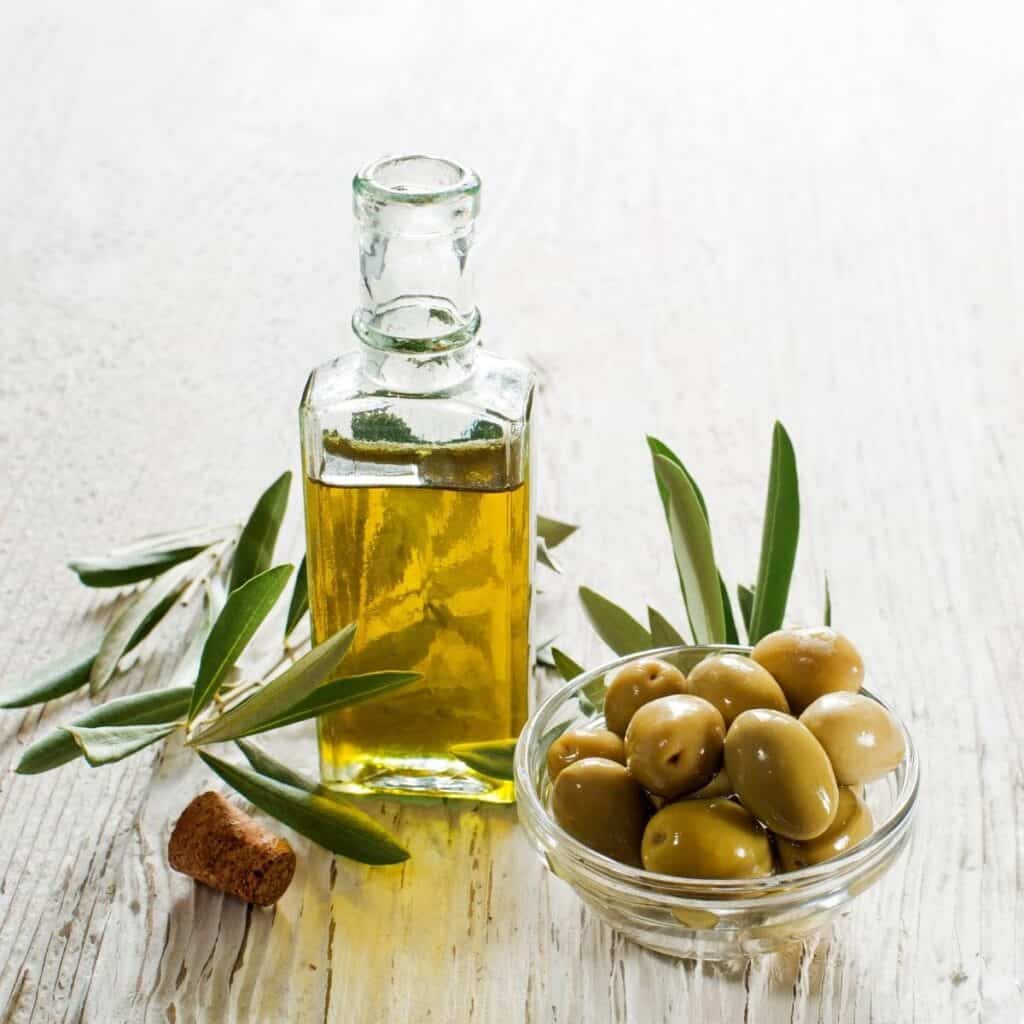 olive oil in a bottle next to a bowl of green olives