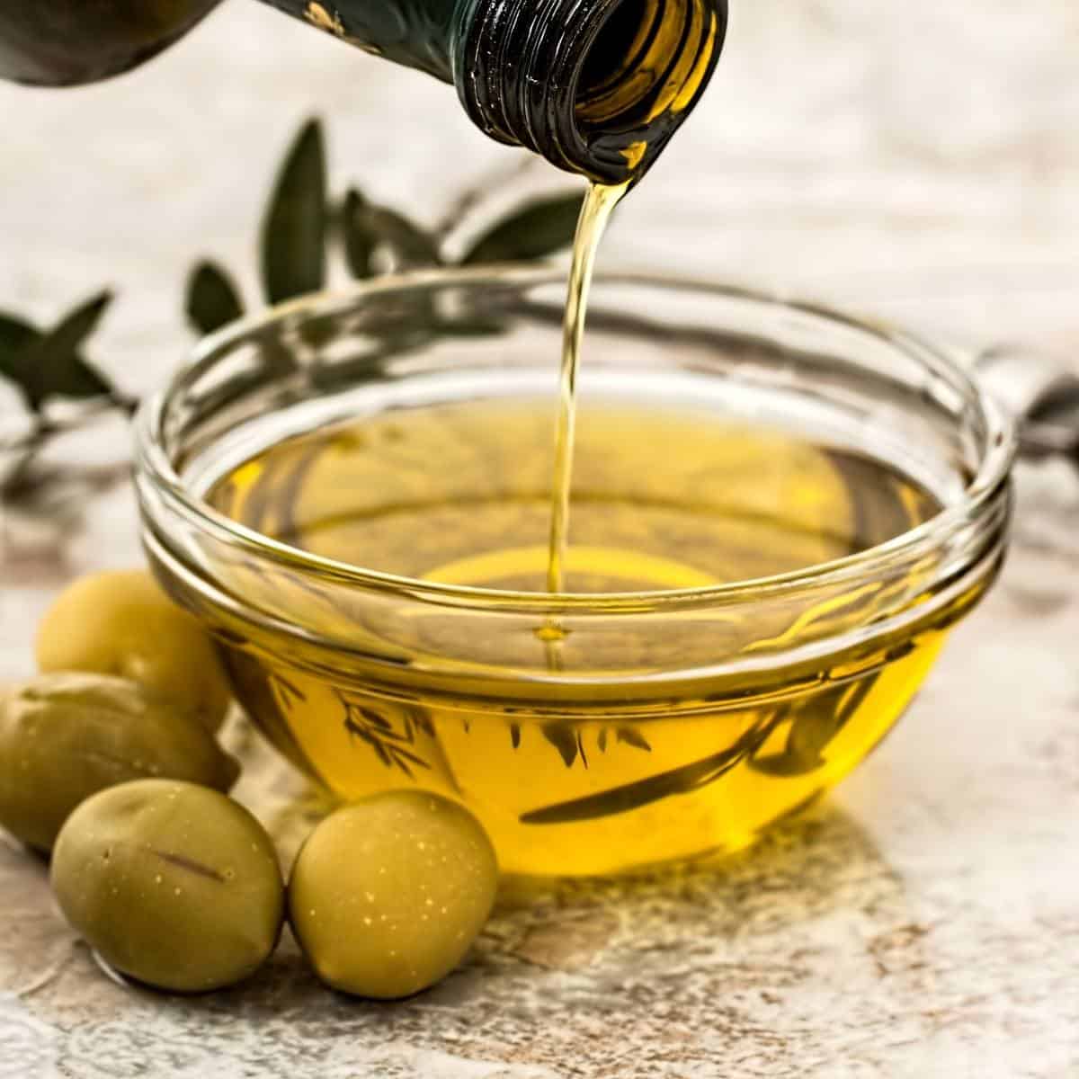 pouring olive oil into a bowl next to green olives