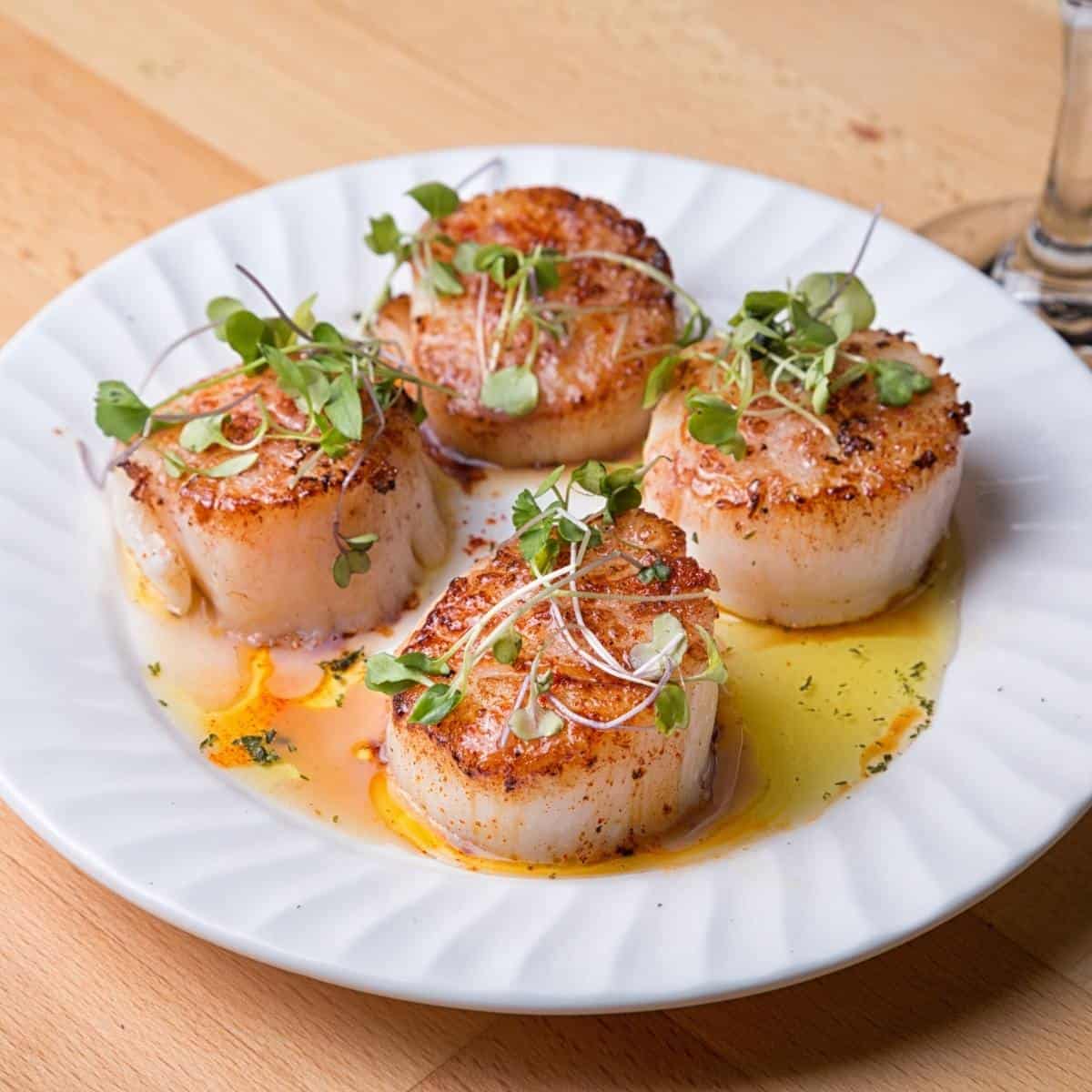 cooked scallops on a white plate in butter with garnish