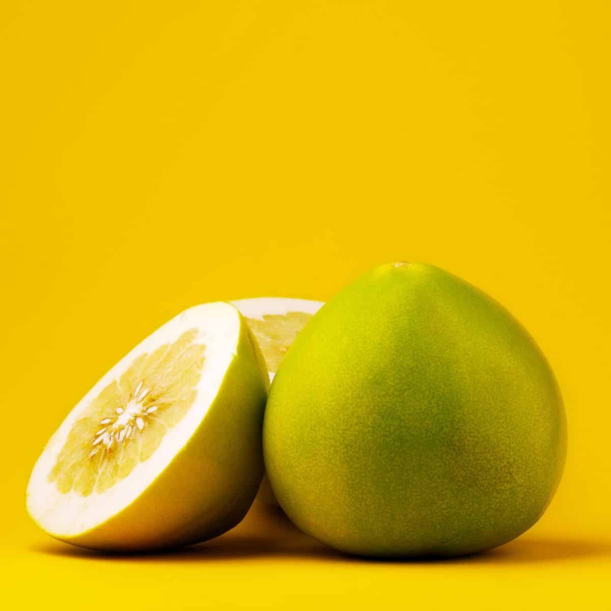 two green pomelos, one has been cut open in half