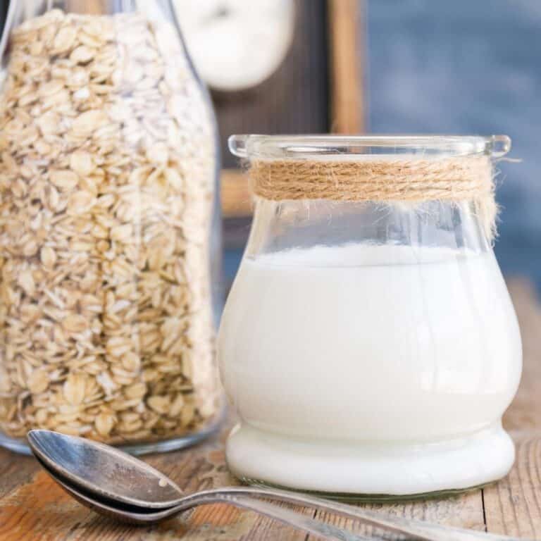 a glass of oat milk next to a tall jar of oats
