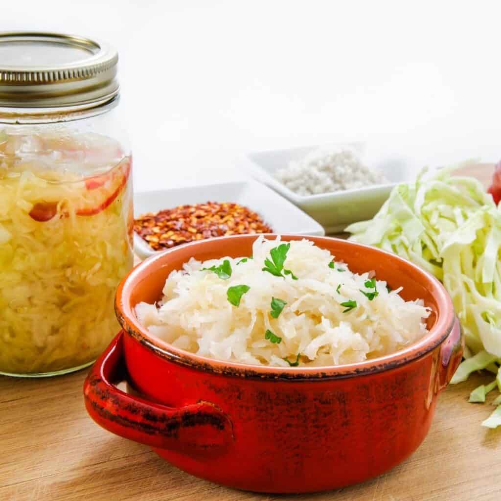 bowl of sauerkraut, next to a jar of sauerkraut and shredded cabbage